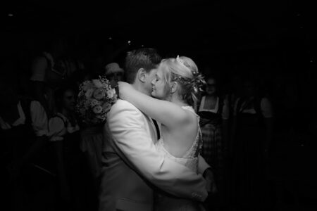 Schwarz-Weiß-Foto: Braut und Bräutigam tanzen Arm in Arm, Wange an Wange, allein angestrahlt im dunklen Saal bei der Hochzeit