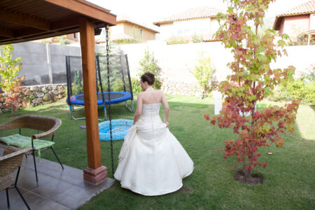 Braut im weißen Hochzeitskleid mit dem Rücken zur Kamera im heimischen Garten