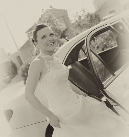 Braut in Hochzeitskleid steht im Retro-Stil vor dem Brautauto, Aufnahme in Sepia