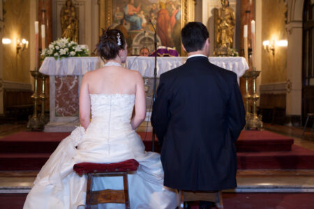 Braut im Hochzeitskleid von hinten, sitzend am Altar während der Trauung in der Kirche
