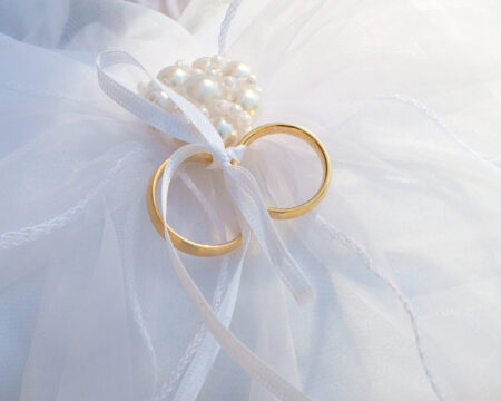 Zwei Eheringe liegen als Detailaufnahme auf einem weißen Hochzeitskissen bereit für die Zeremonie.