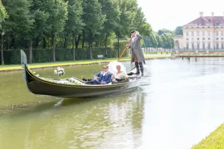 Verliebtes Hochzeitspaar auf einer Gondel vor Schloss Unterschleißheim, umgeben von Wasser und Parklandschaft